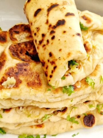 fluffy naan bread stacked on a plate with the top one rolled over. Naan bread recipe