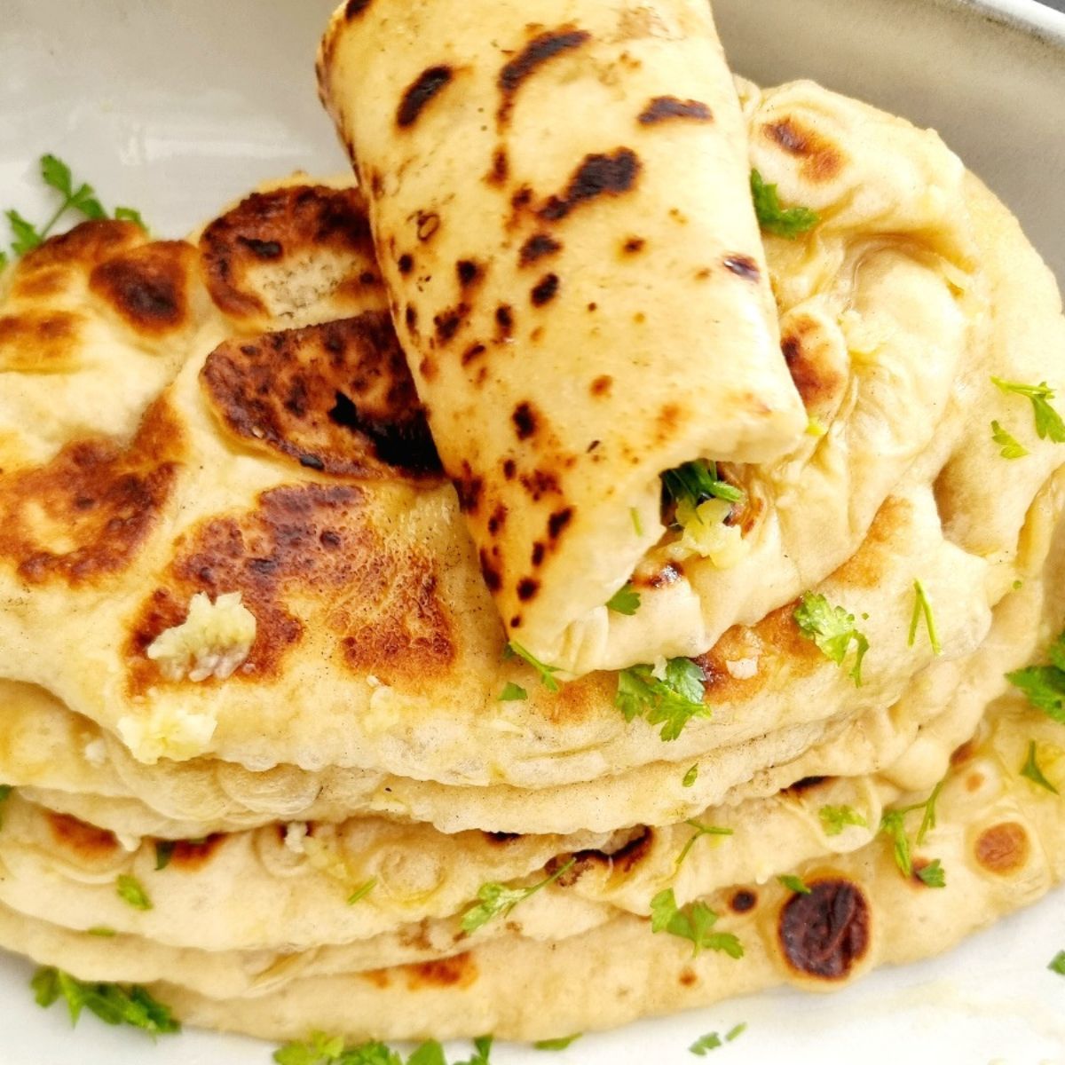 fluffy naan bread stacked on a plate with the top one rolled over. Naan bread recipe