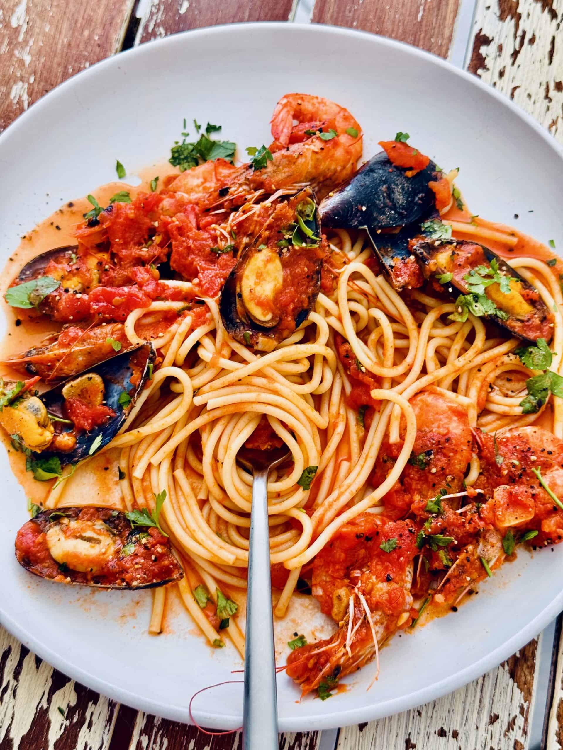 seafood marinara on a white plate with spaghetti swirled around a fork