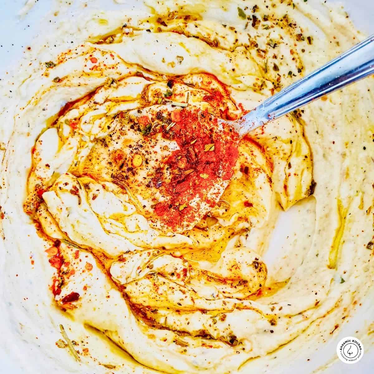 rich and creamy mascarpone cheese dip with spices, herbs and olive oil on a plate with a spoon dipped in.