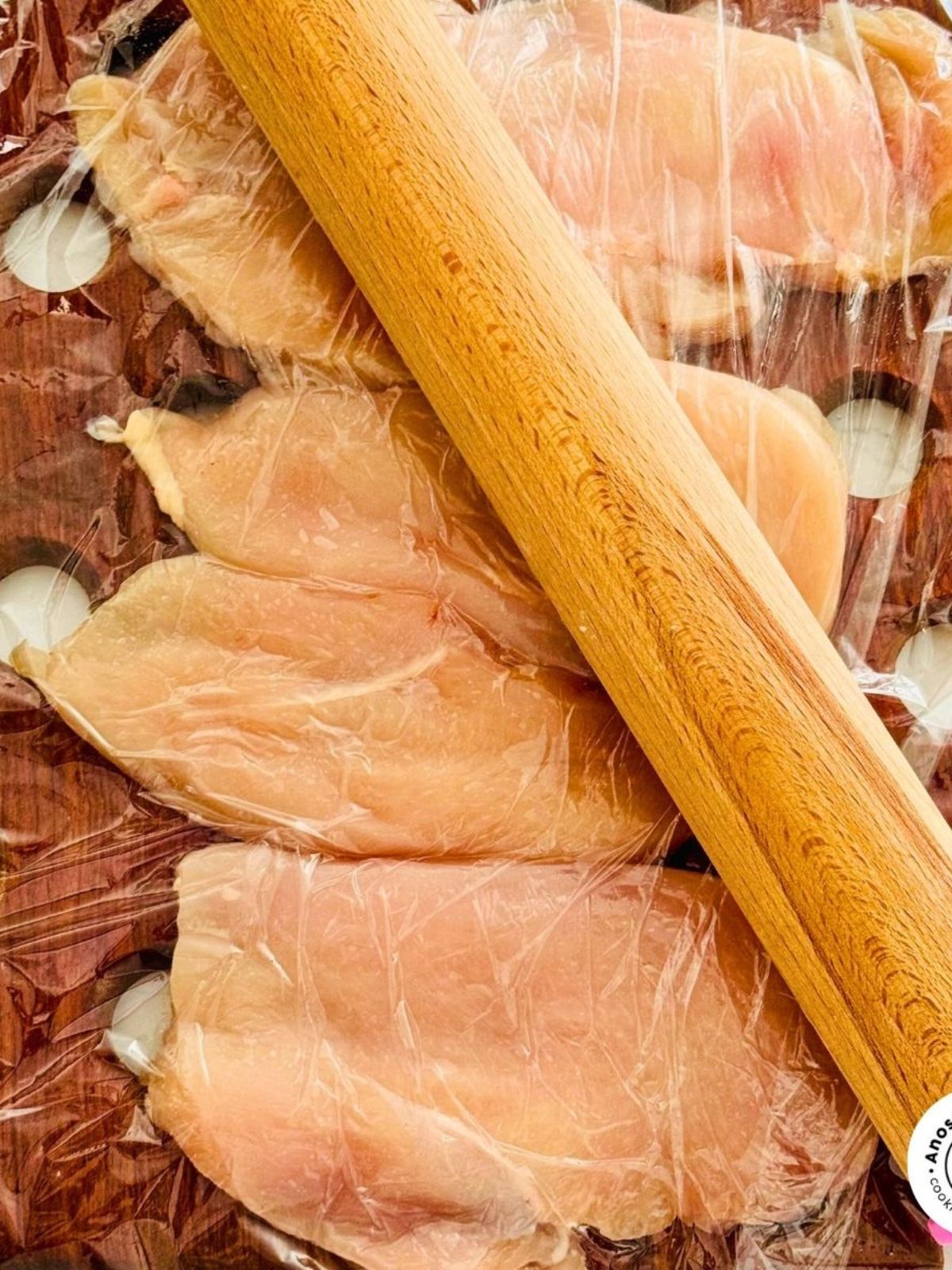 Chicken breasts covered in plastic wrap and tenderized with a rolling pin.