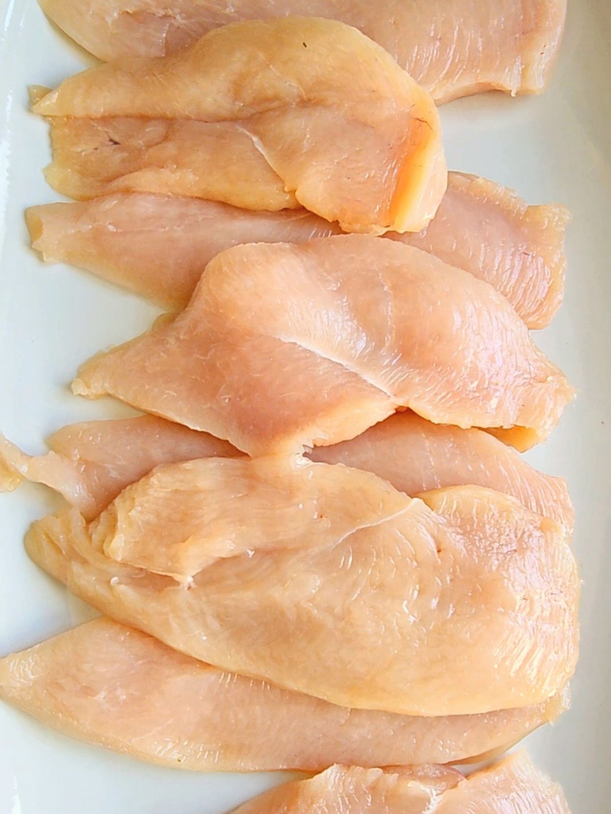 Thinly sliced chicken breast cutlets arranged on a plate before cooking.