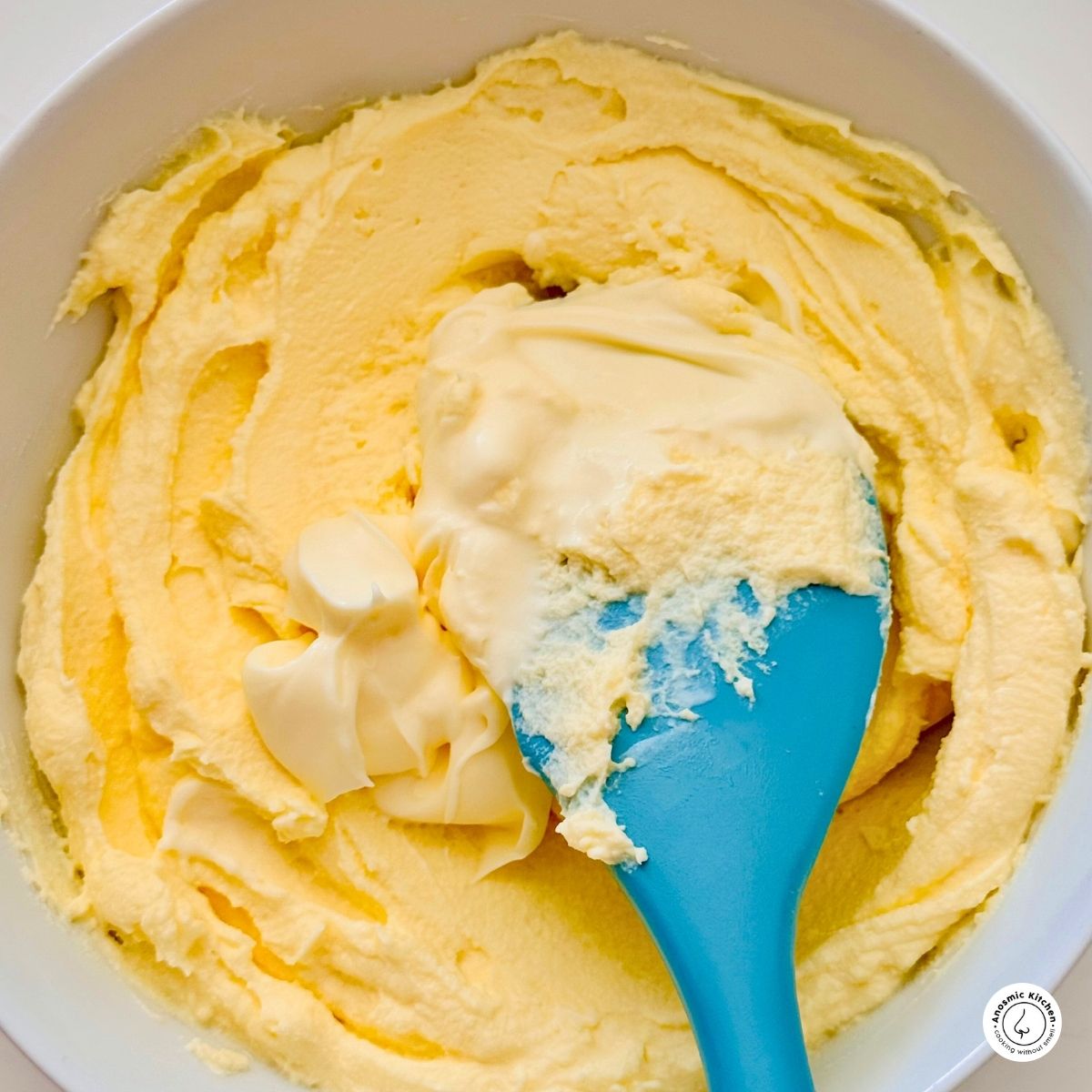 mascarpone being mixed with sour cream with a blue spatula in a white bowl