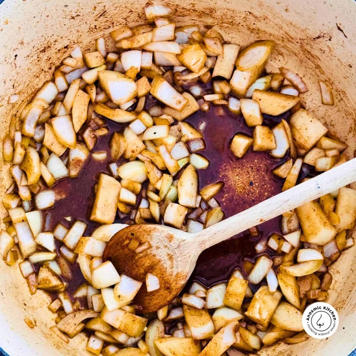 chunky onion pieces frying in a pot with a wooden spoon in the pot for mixxing