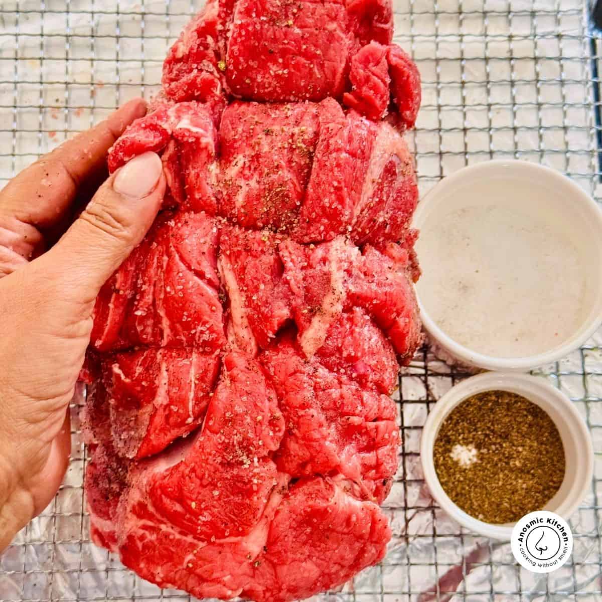 rolled beef chuck with salt pepper and olive oil and a hand holding the beef.