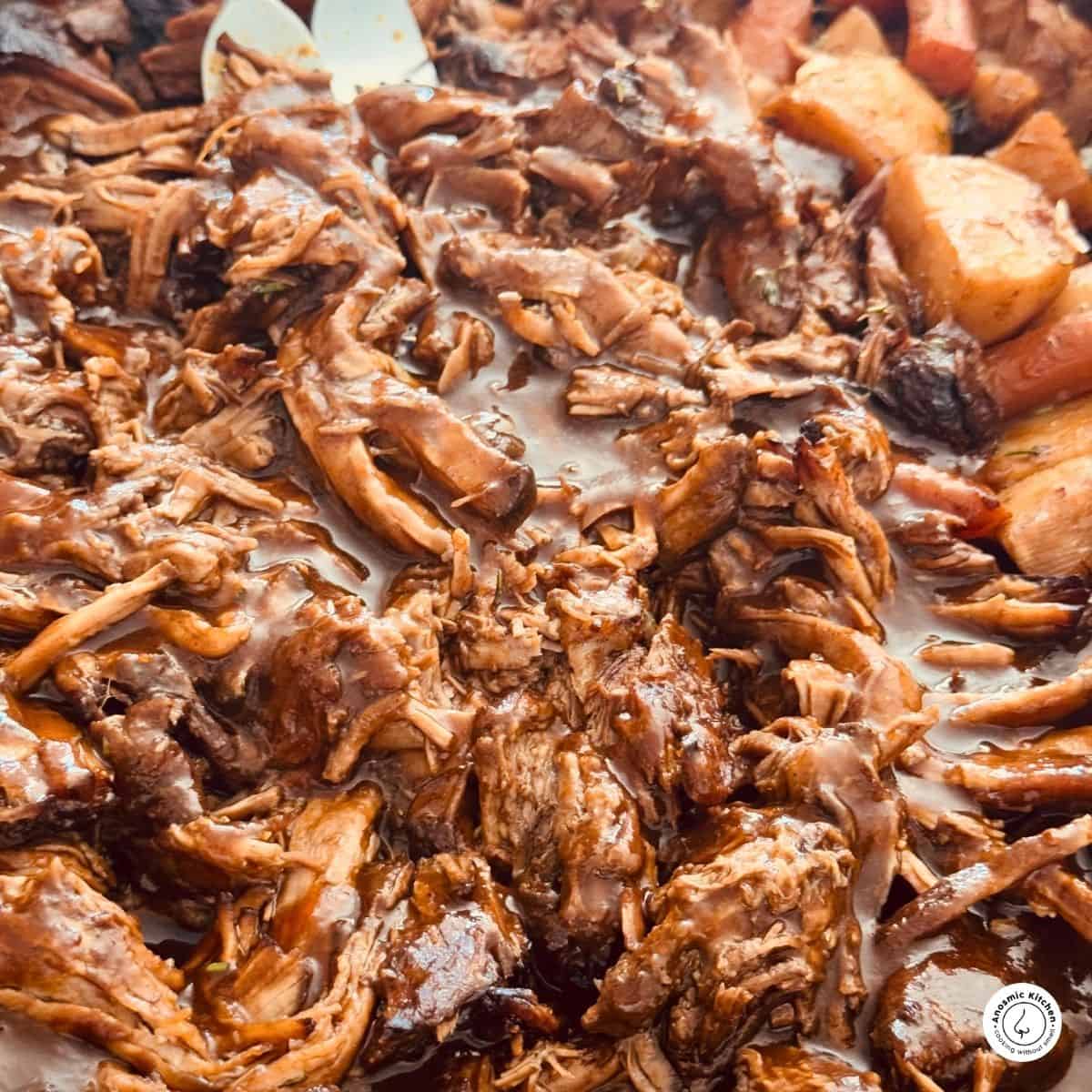 beef chuck roast meat pulled apart with sauce over it, potatoes on the side and 2 forks.