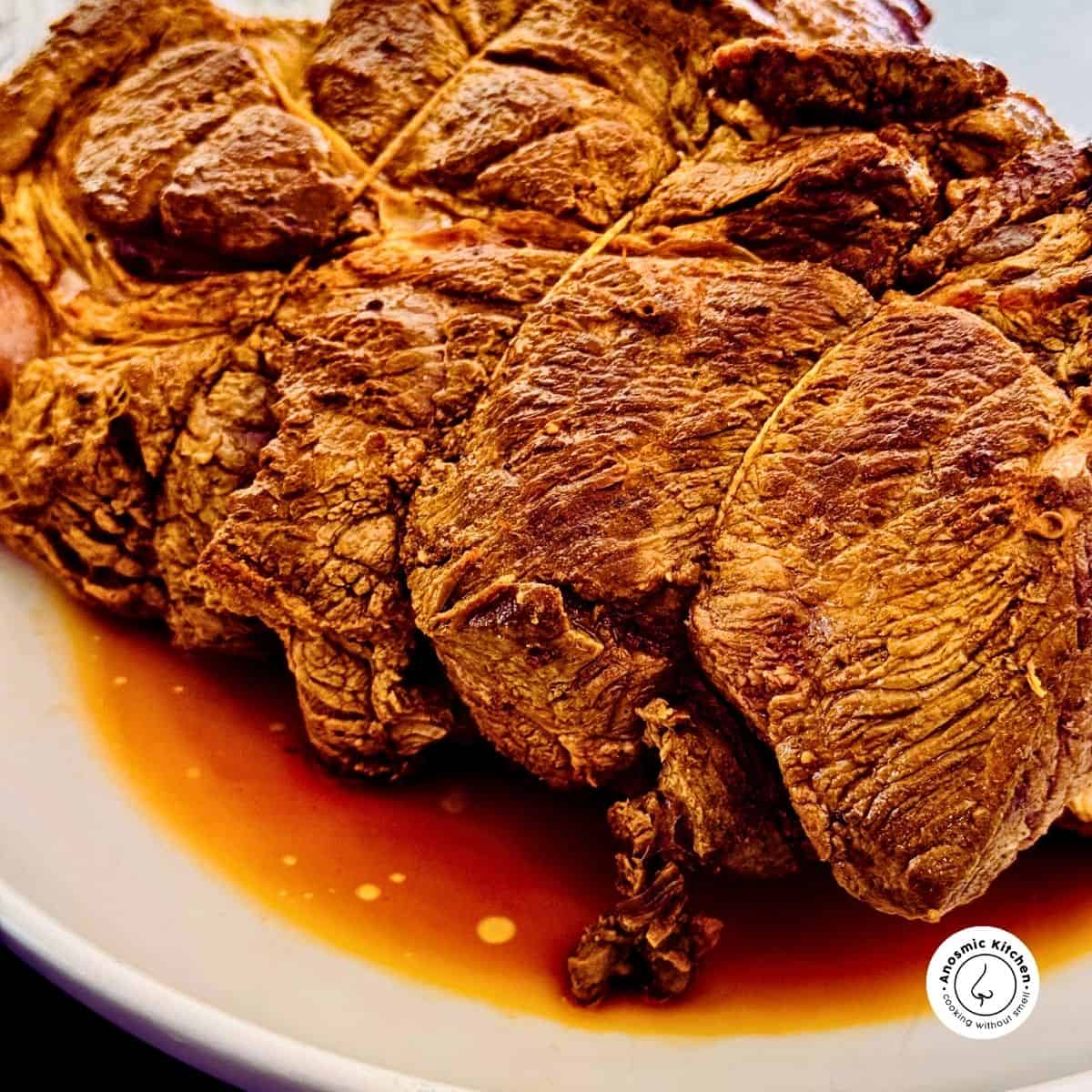 seared beef chuck roast resting on a white plate with the resting juices.