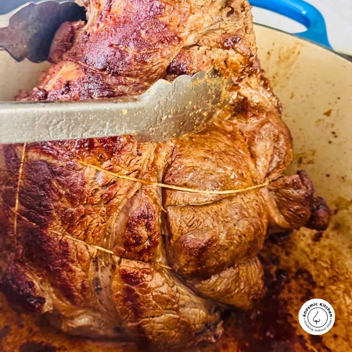 beef chuck roast being seared in a dutch oven and held with tongs