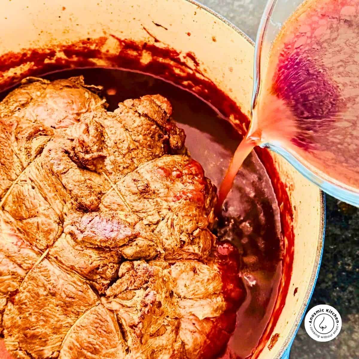 red wine being poured into pot roast in a pot