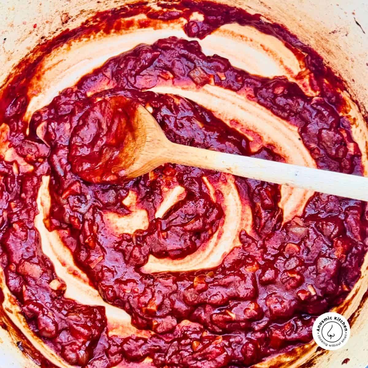 onions and tomato paste in a pot with a wooden spoon