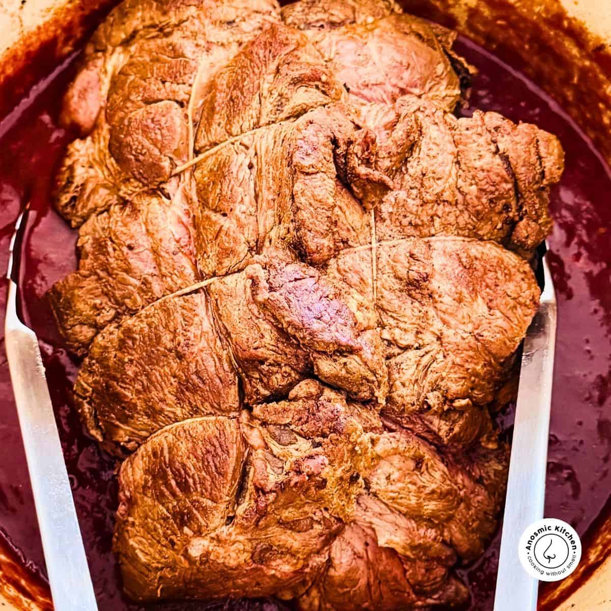 chuck roast being held with tongs inside a large pot