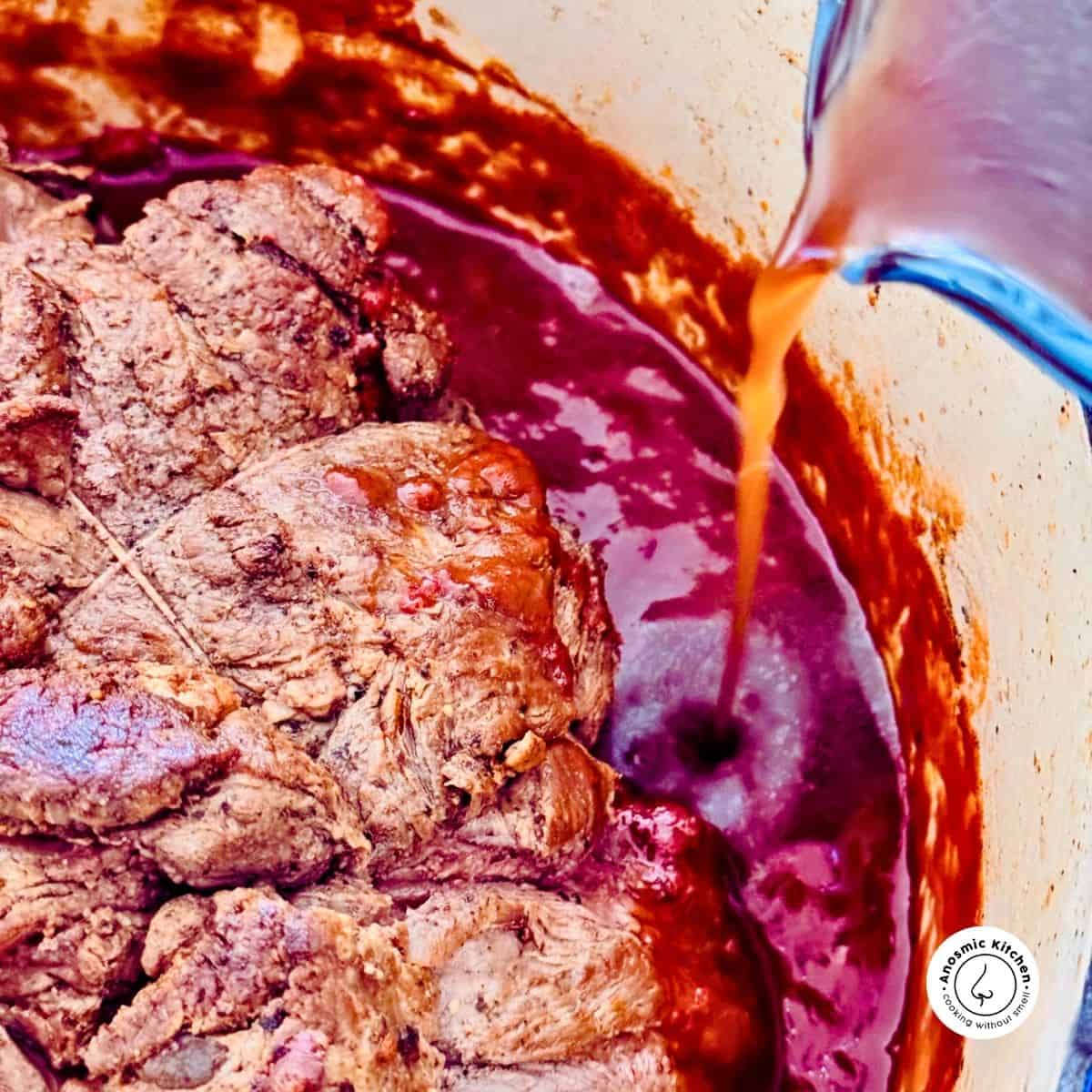 beef stock being poured into a pot of beef and tomato sauce