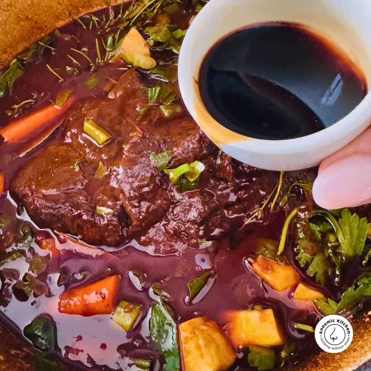 worcestershire sauce being poured into a pot roast with veggies and herbs