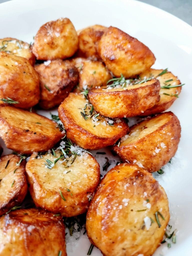 golden brown roast potatoes piled on a dish with fresh herbs.