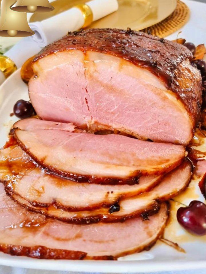 large gammon roast, partly sliced with cherries on the side as garnish, white serviette and xmas decor in the background.