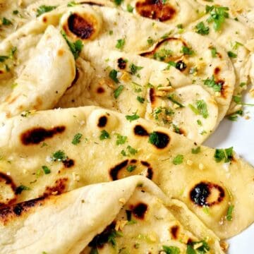 soft and fluffy naan bread piled high on aplate with a sprinkle of chopped fresh herbs.