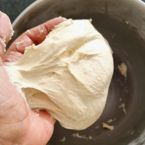 naan bread dough on a hand being transferred to flour surface.