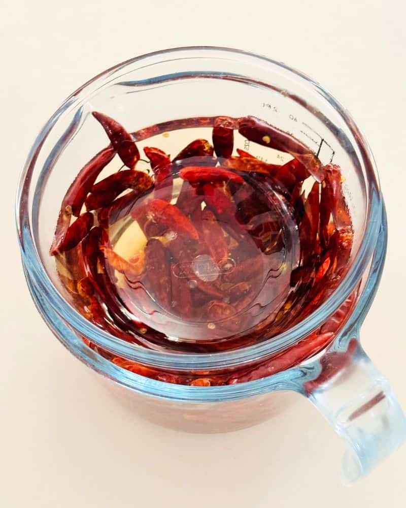 dried chillies soaking iin water in a measuring jug with a bowl over them.