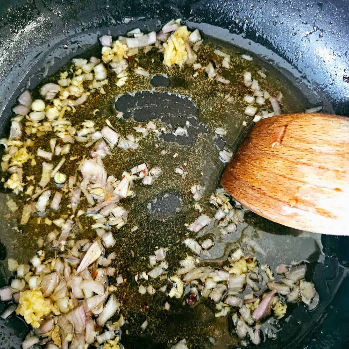 Minced garlic and diced shallots sautéing in a pan with oil for creamy bacon pasta