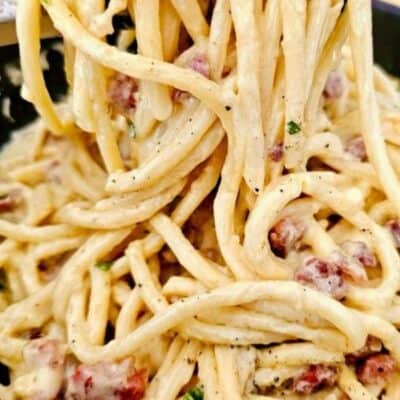 Creamy bacon pasta lifted with a fork, falling into a rich, silky heap of sauce-coated noodles