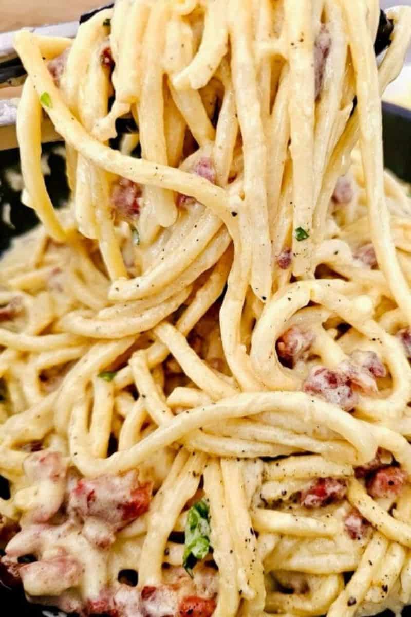 Creamy bacon pasta lifted with a fork, falling into a rich, silky heap of sauce-coated noodles