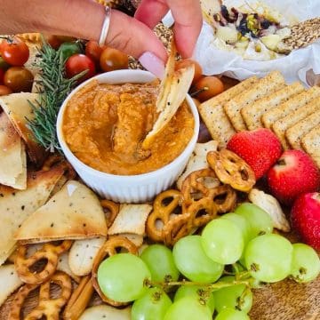Charcuterie board with crackers, fruit, cheese, pretzels, and dip.