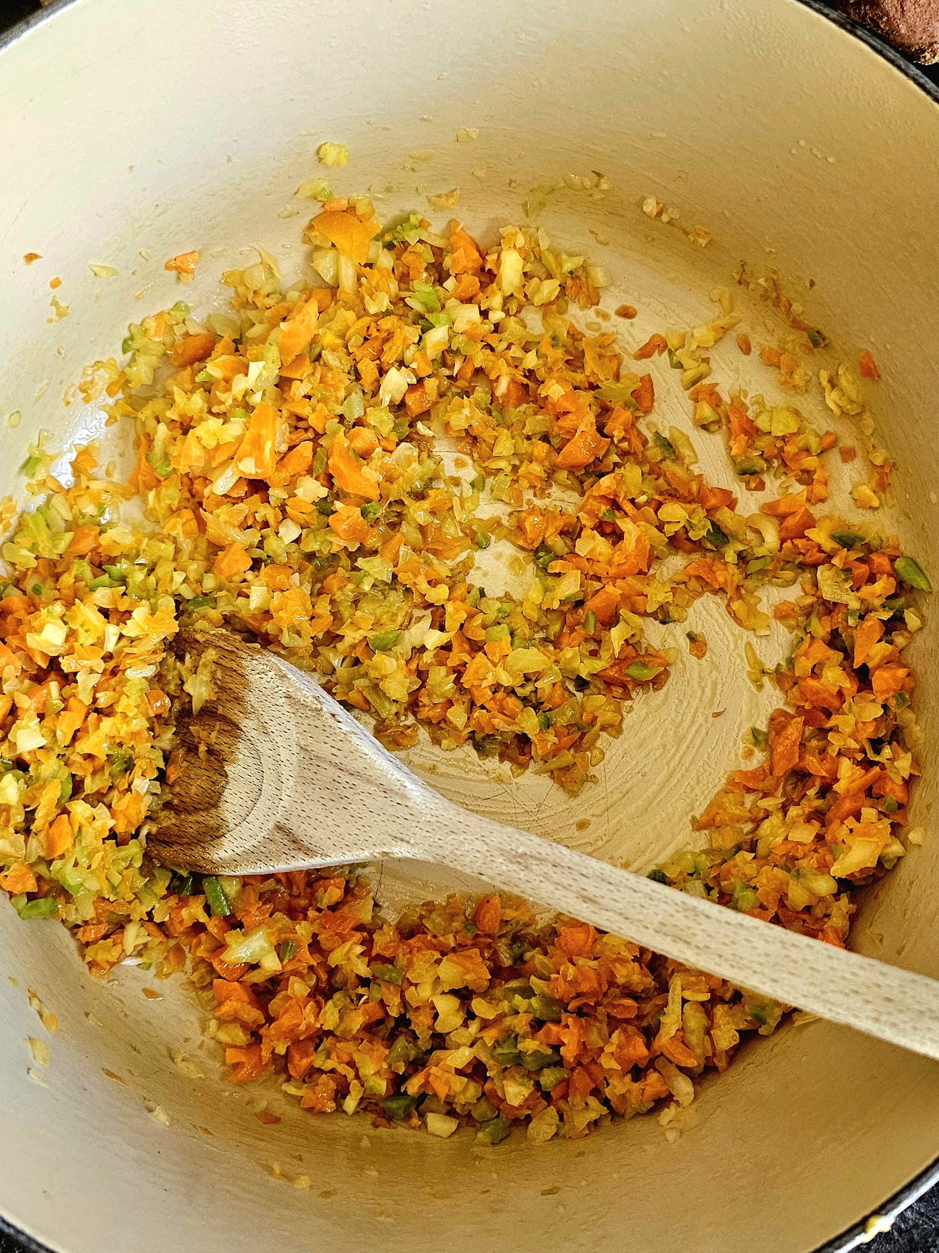 diced carrots, celety and onion in a pan or pot cooking with a wooden spoon inside for stirring