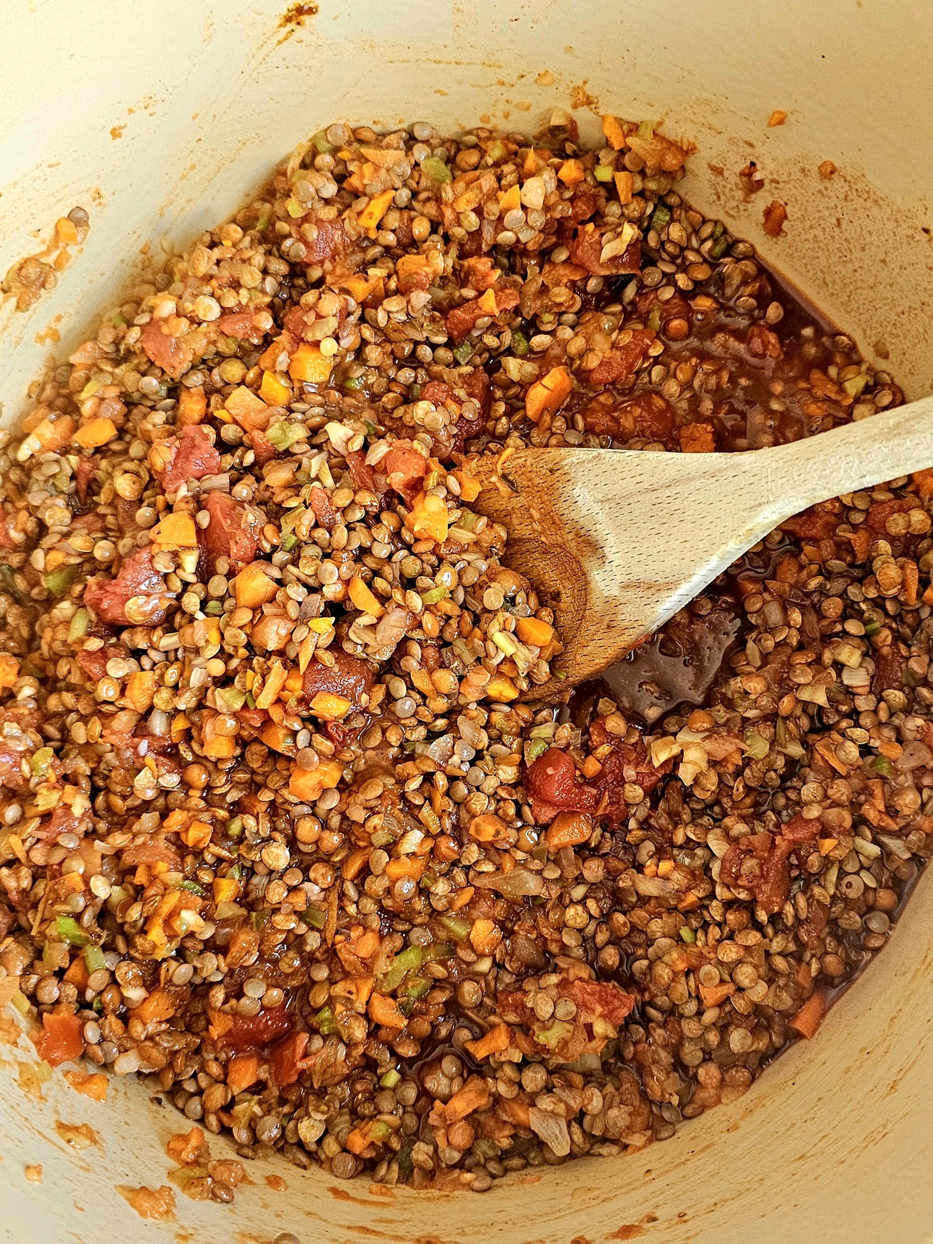 lentils with a soffritto and tomatoes being stirred with a wooden spoon as it cooks