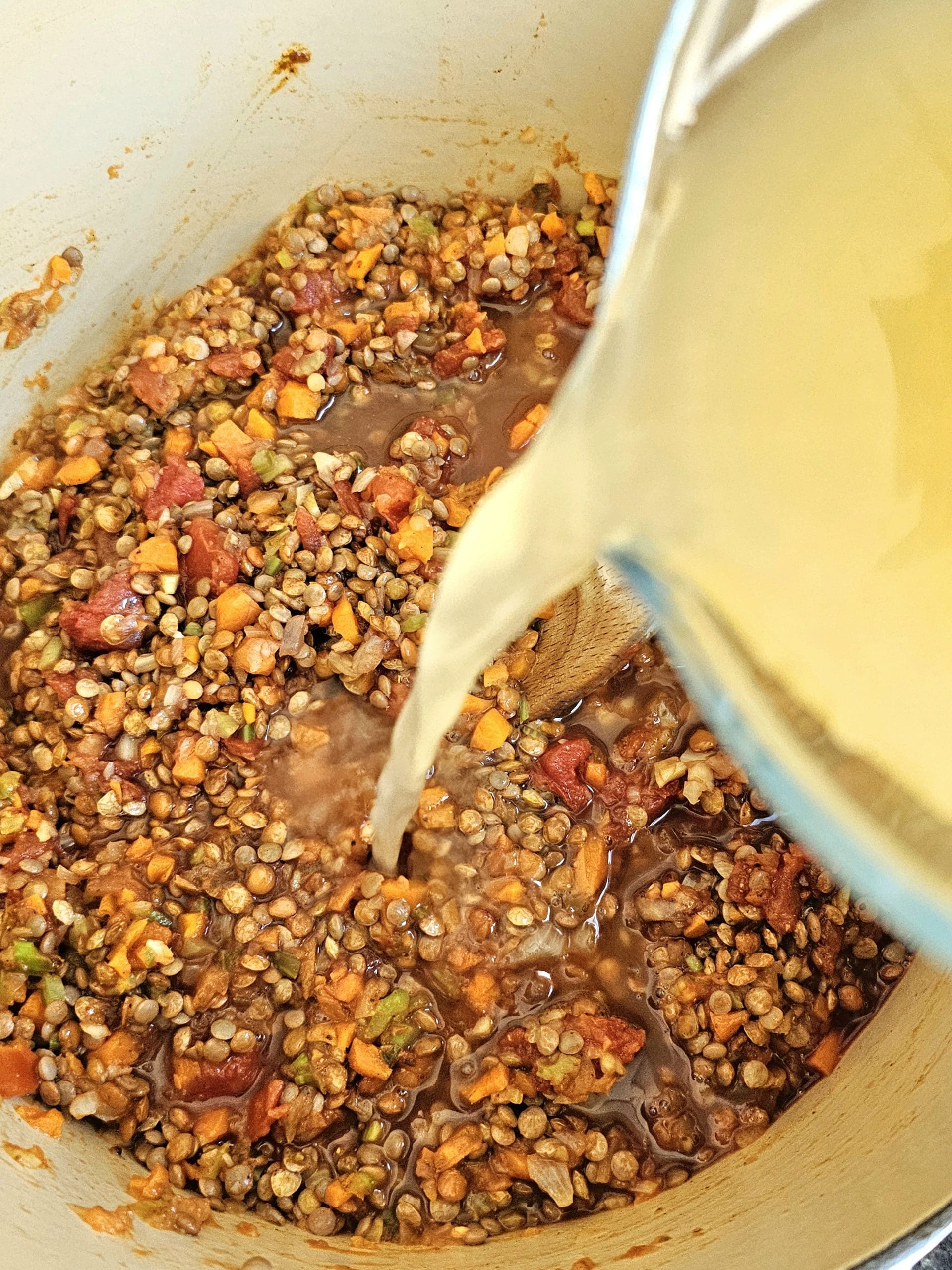 stock being poured into a pot of lentils as it cooks