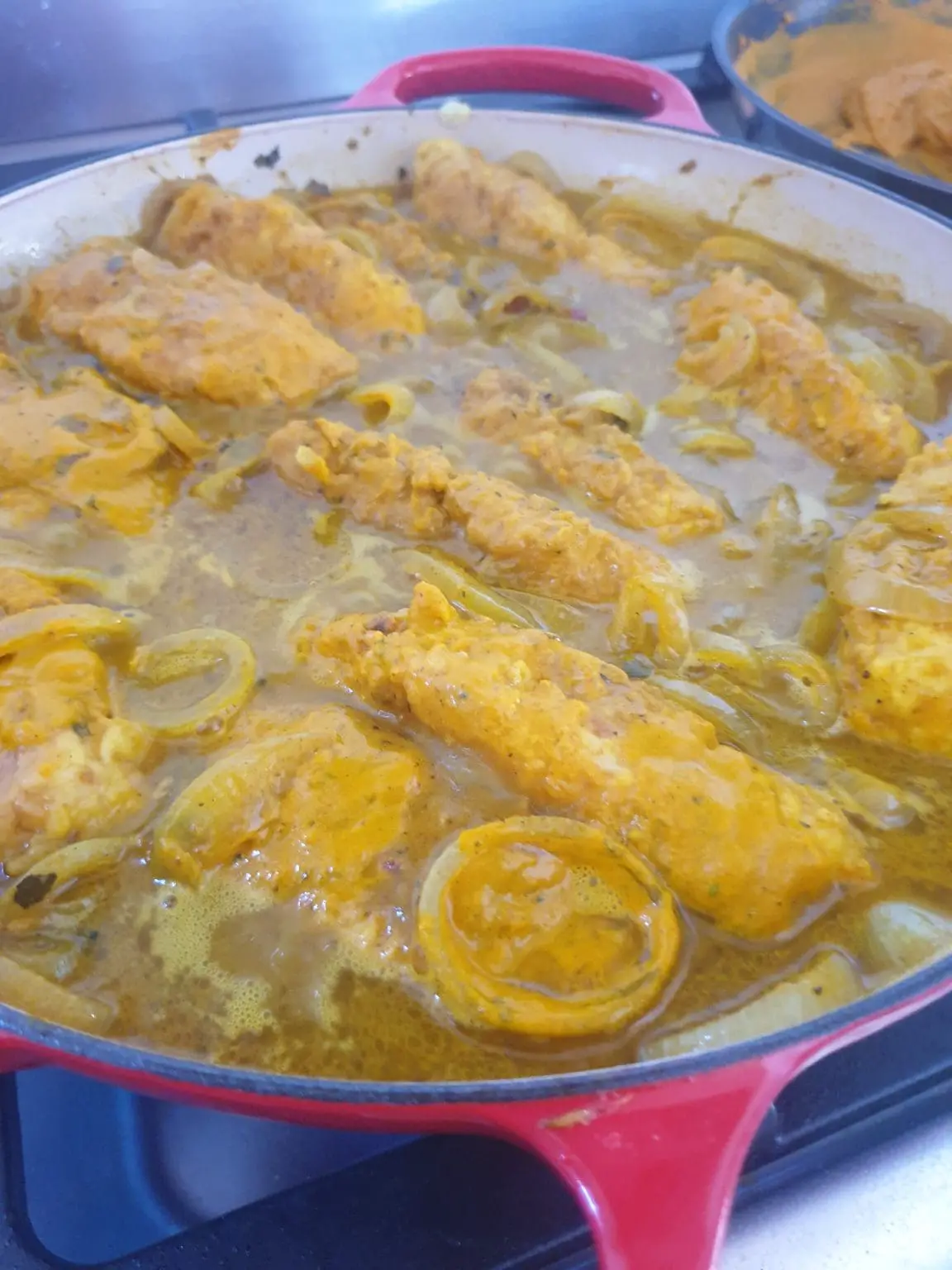 Fried fish pieces simmering with onions in spiced curry sauce