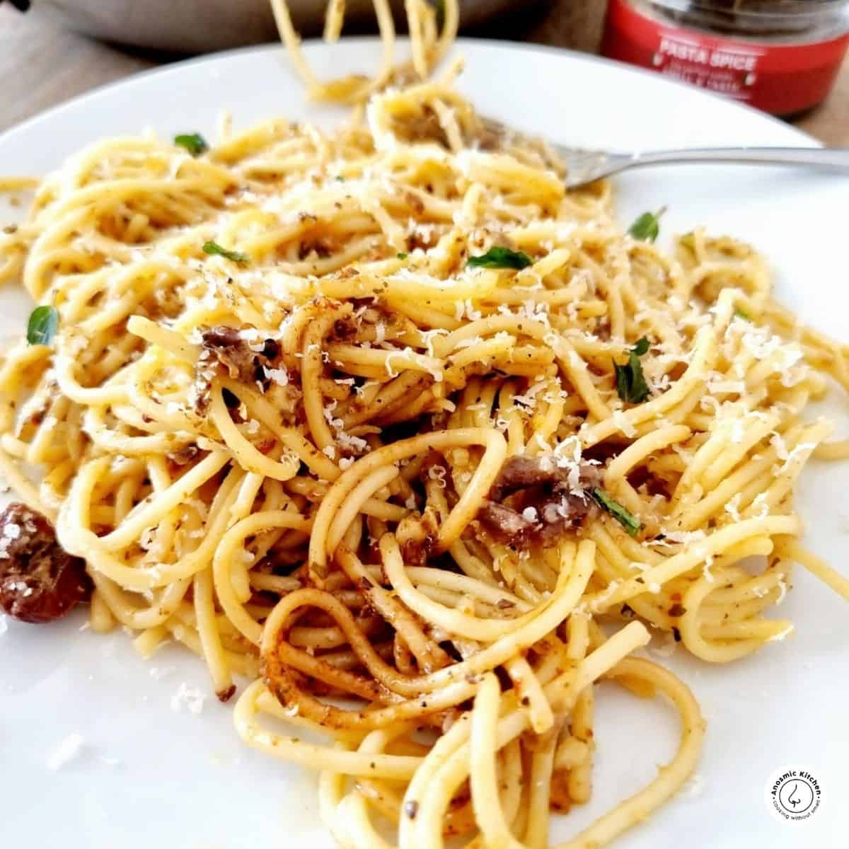 spaghetti anchovy pasta on a plate slightly lifted with a fork