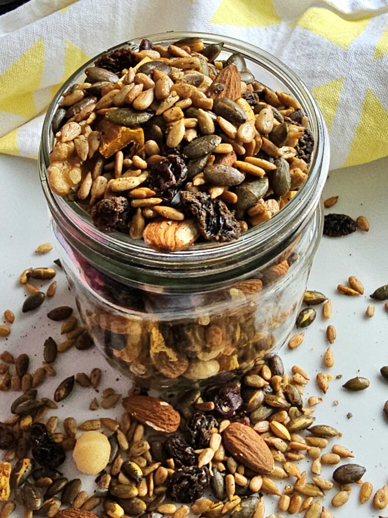 air fryer pumpkin seed mix (trail mix) in a mason jar with some of the trail mix on the table around the jar with a kitchen towel in the background.