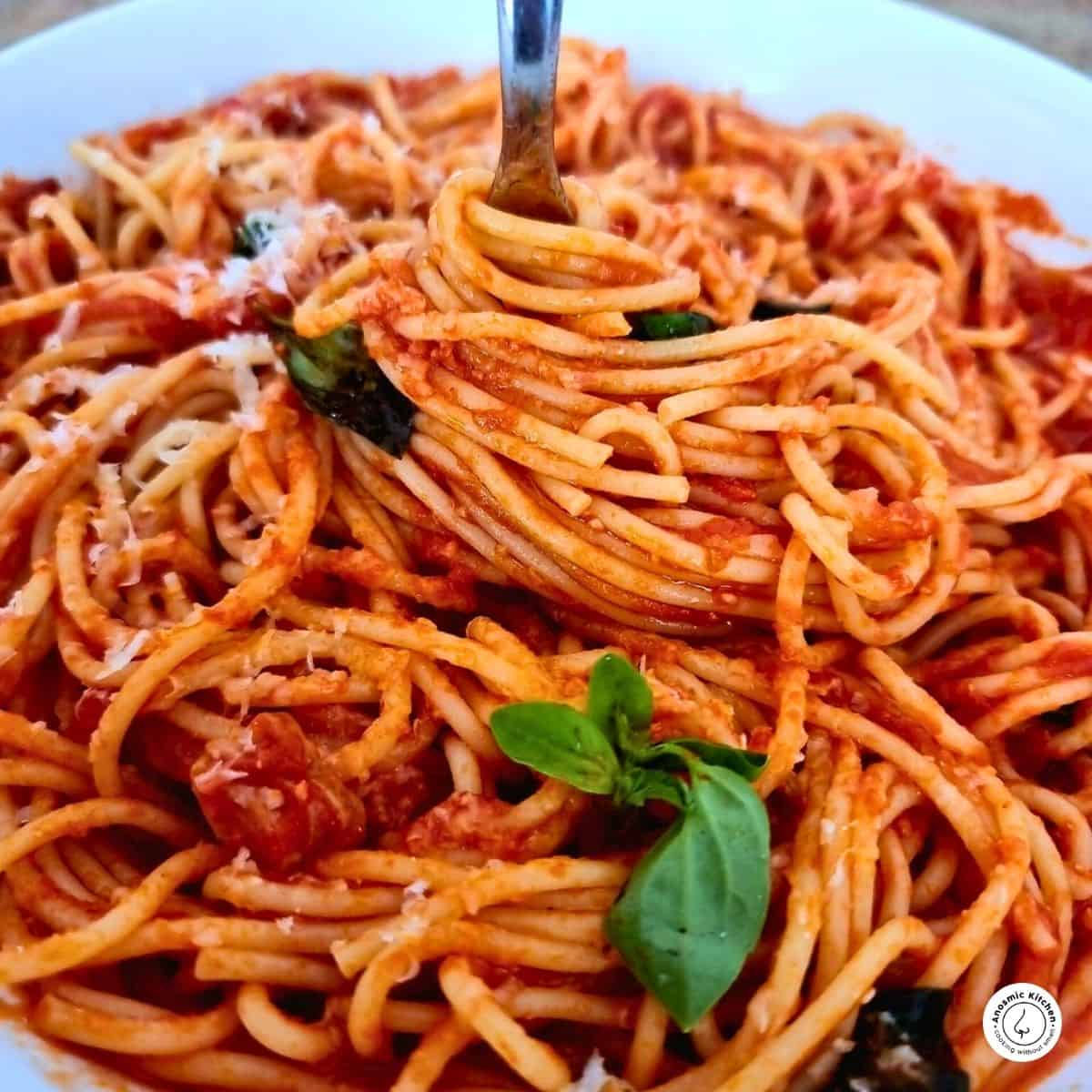 Penne all'arrabbiata (spicy pasta) all swirled around with a fork in the middle and fresh basil for garnish on a white plate
