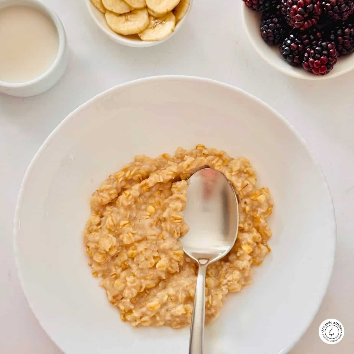 cooked rolled oats in a white small bowl with a spoon and fresh fruit