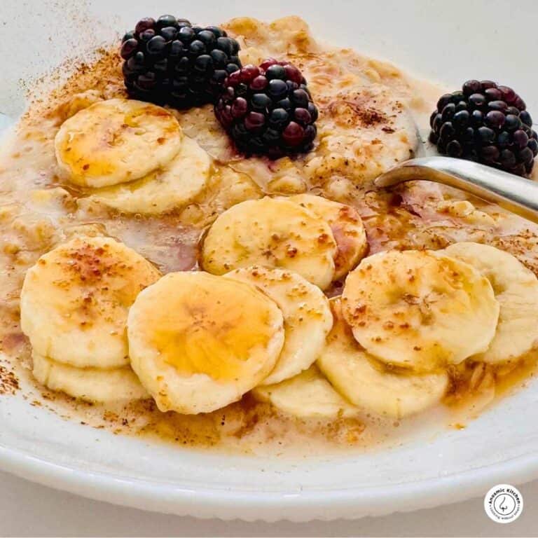 cooked oats with sliced banana, fresh blackberries, cinnamon, honey and a spoon in a white small bowl