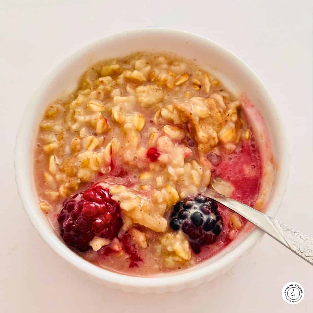oatmeal with fresh fruit in a small white bowl and spoon on a white table