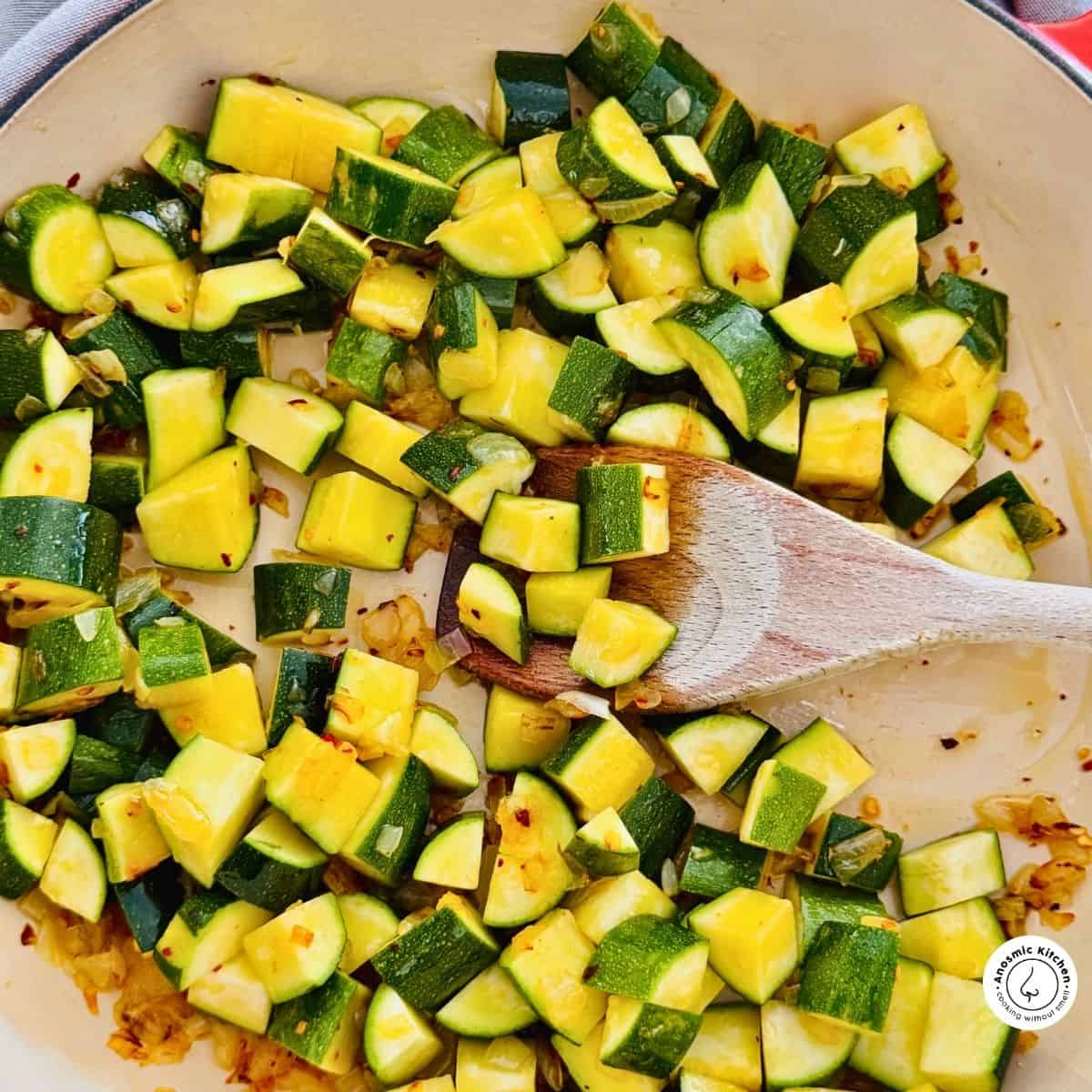 diced zucchini in pan with wooden spoon