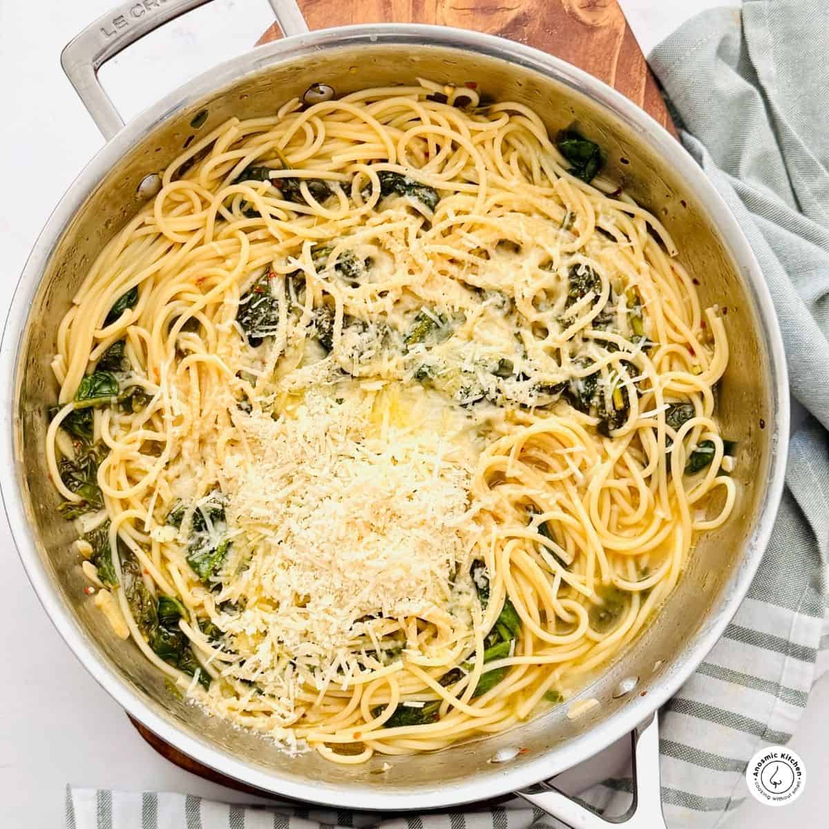 spaghetti spinach lemon and parmesan cheese in a skillet with kitchen kitchen towel underneath