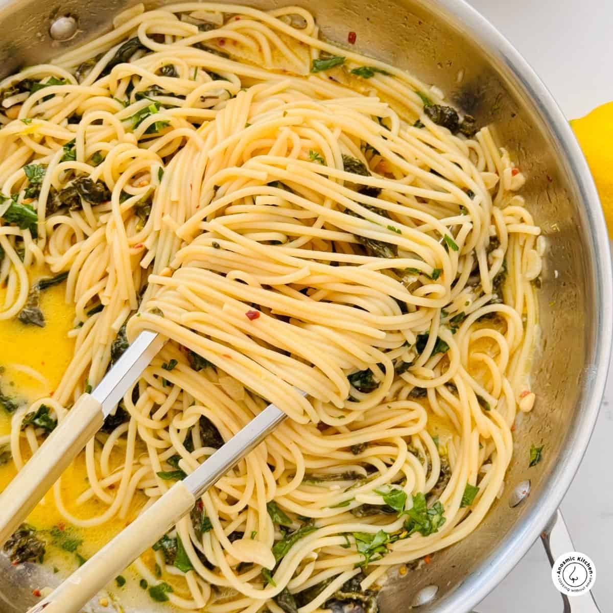 spaghetti spinach lemon and parmesan cheese in a skillet with a pair of tongs holding the spaghetti