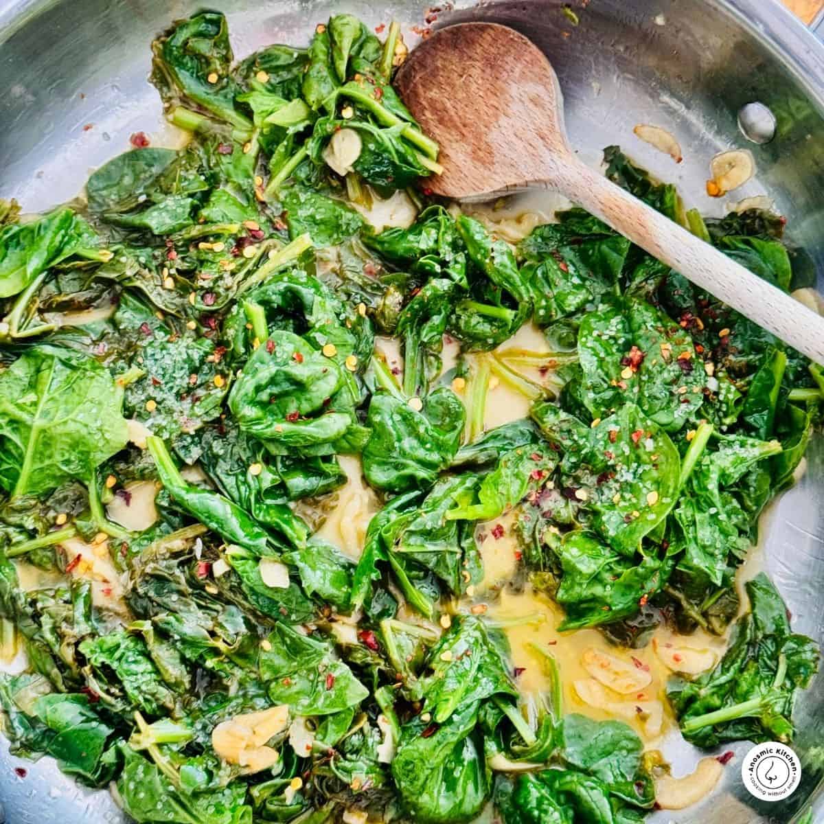 spinach in a pan with a wooden spoon