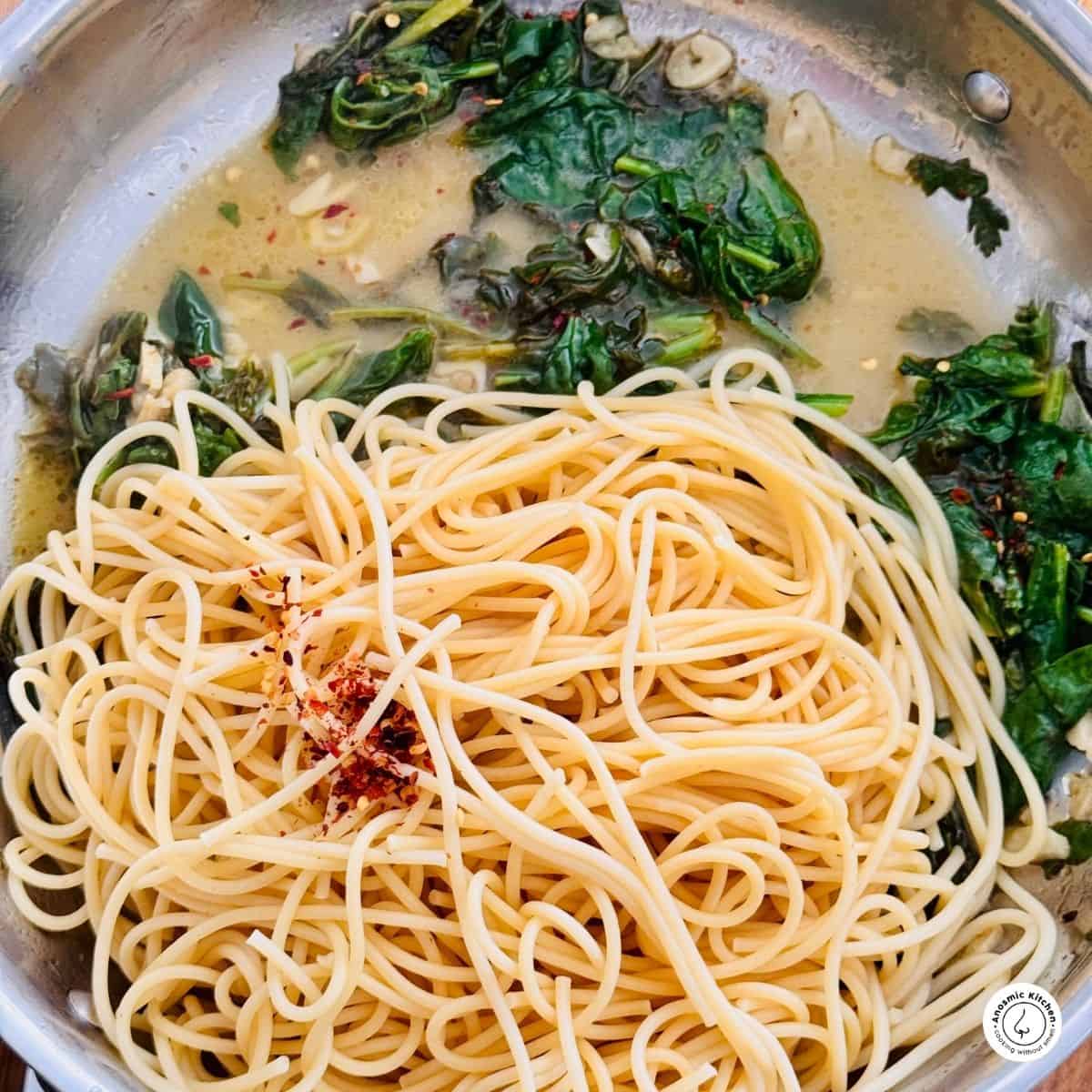 spaghetti and spinach in a skillet with oil