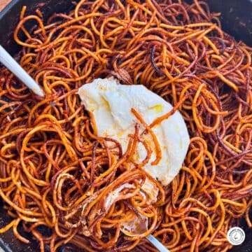 spaghetti all'assassina with burrate in a skillet with a silver spoon and fork