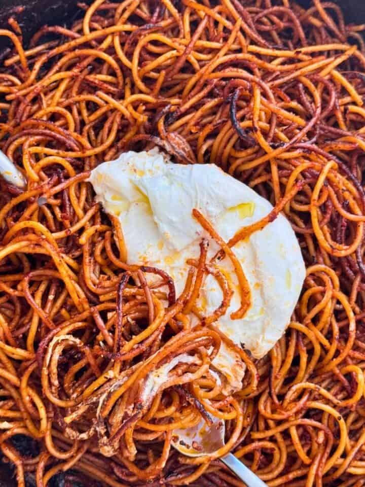 spaghetti all'assassina with burrate in a skillet with a silver spoon and fork