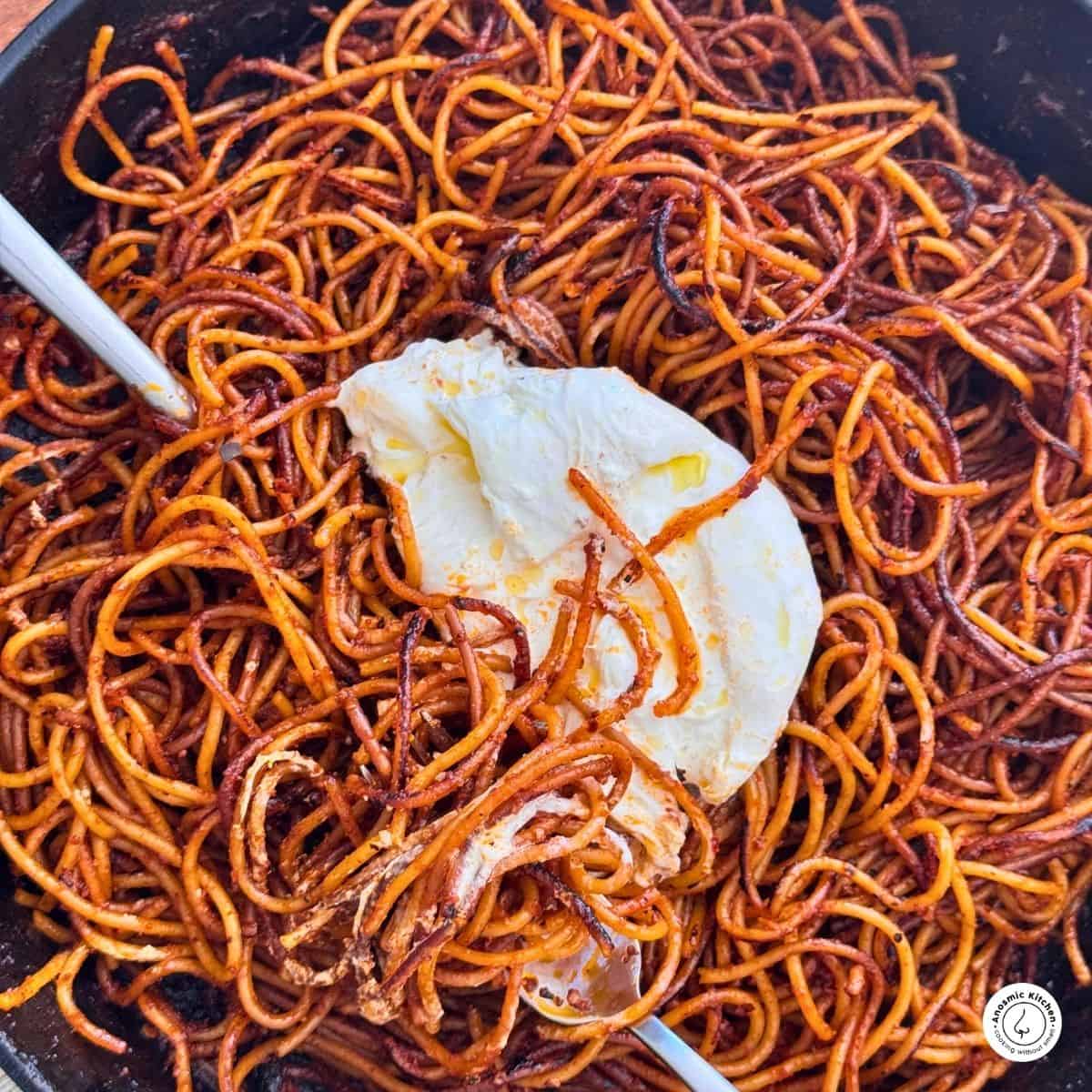 spaghetti all'assassina with burrate in a skillet with a silver spoon and fork