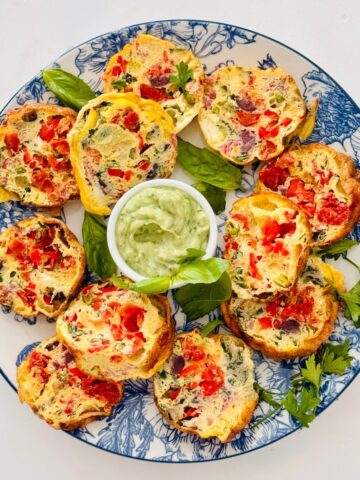 mediterranean egg muffins sliced open and placed on a blue and white floral round plate with a green basil ricotta pesto.