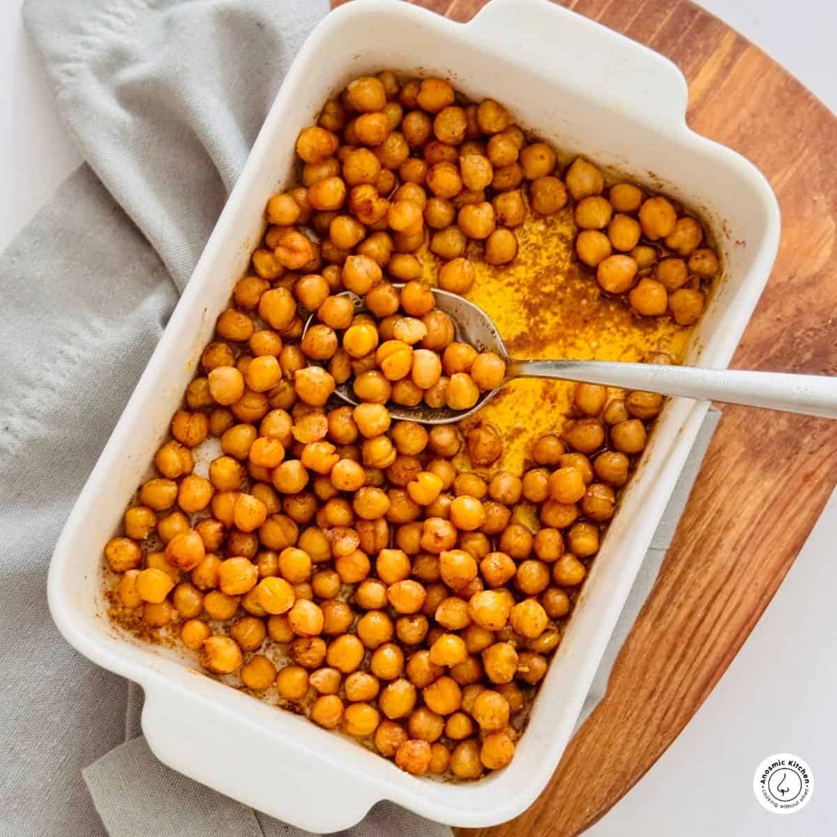 air fryer chickpeas in a white ceramic dish over a board and gray dish towel. Silver spoon inside the dish.