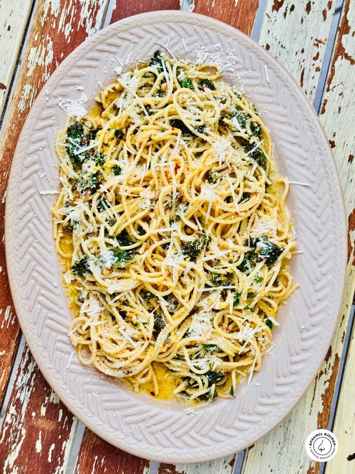 spinach lemon pasta with parmesan cheese on a brown platter over an old wooden table