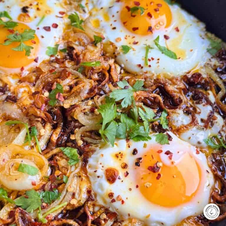 Fried eggs with caramelized onions in a skillet, garnished with fresh parsley