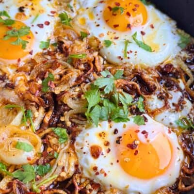 Soft fried eggs with caramelized onions, garnished with fresh parsley in a one-pan breakfast.