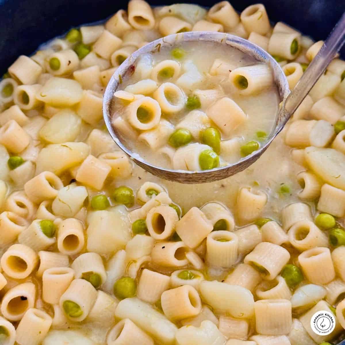 One-pot pasta with peas and potatoes, scooped with a ladle from a soup pot (close up shot)